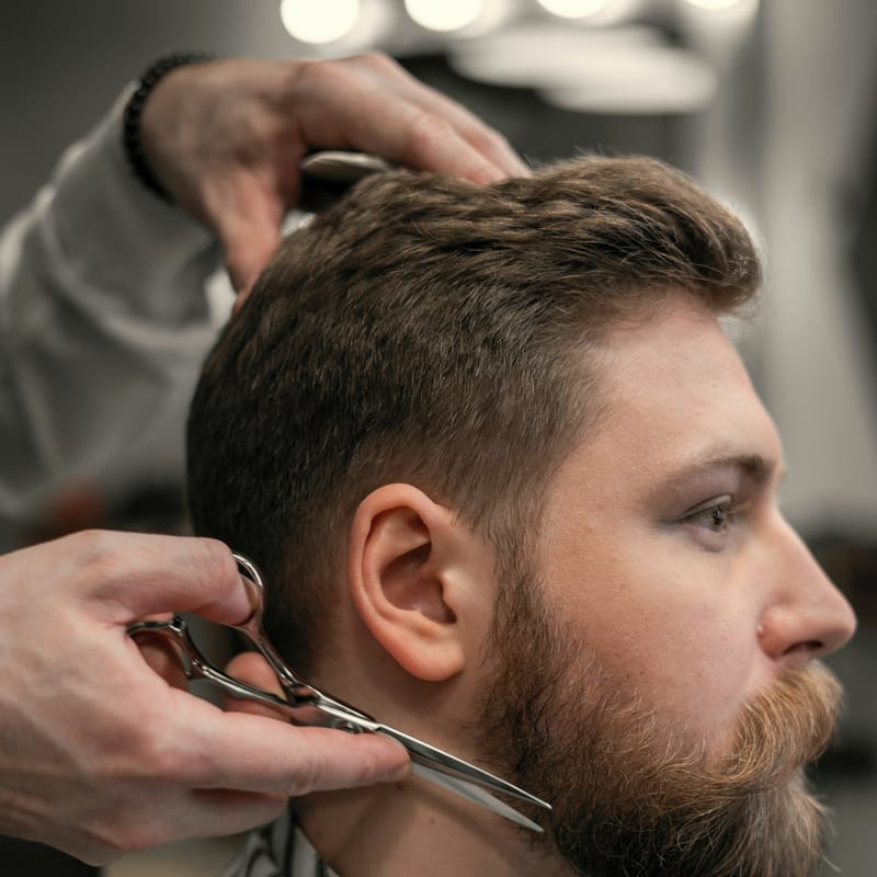 Barbeiro aparando a barba de um cliente com tesoura