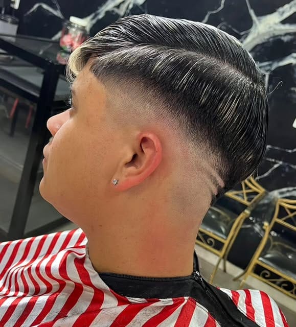 Cliente de perfil com corte social penteado para trás e degradê baixo, na capa listrada vermelha e branca da barbearia